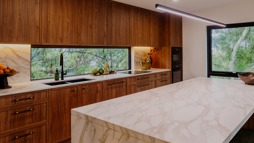 Modern kitchen with wooden cabinets, marble island, and large windows.
