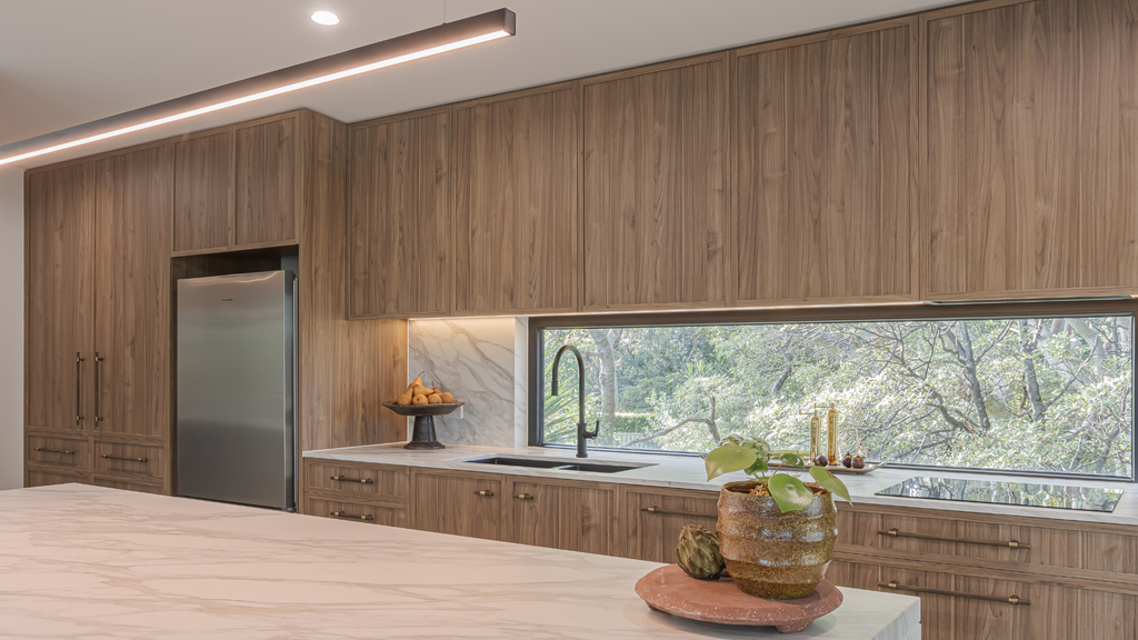 Modern kitchen with wooden cabinets and a view of trees outside.