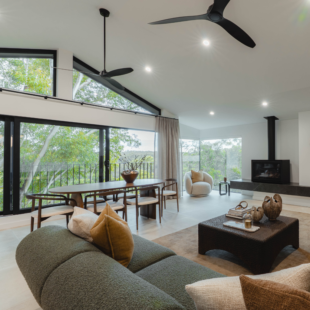 Modern living room with a green sofa, wooden coffee table, and large windows overlooking trees.