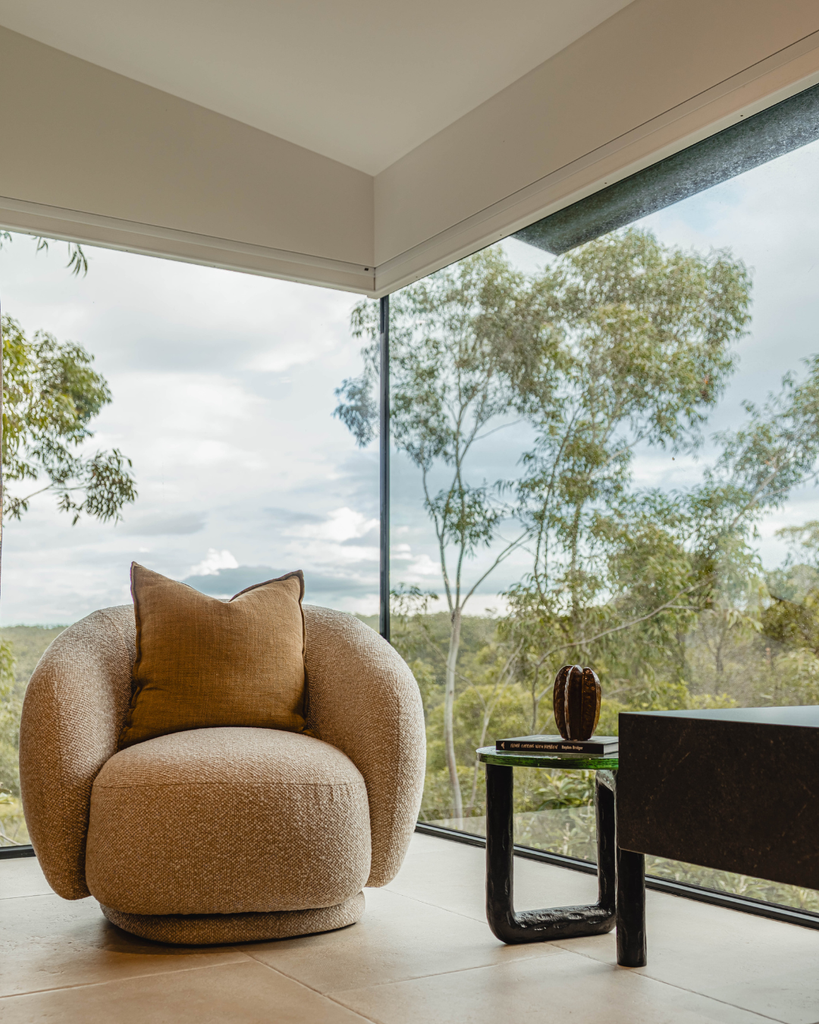 Brown armchair with a pillow on a patio with large windows overlooking trees